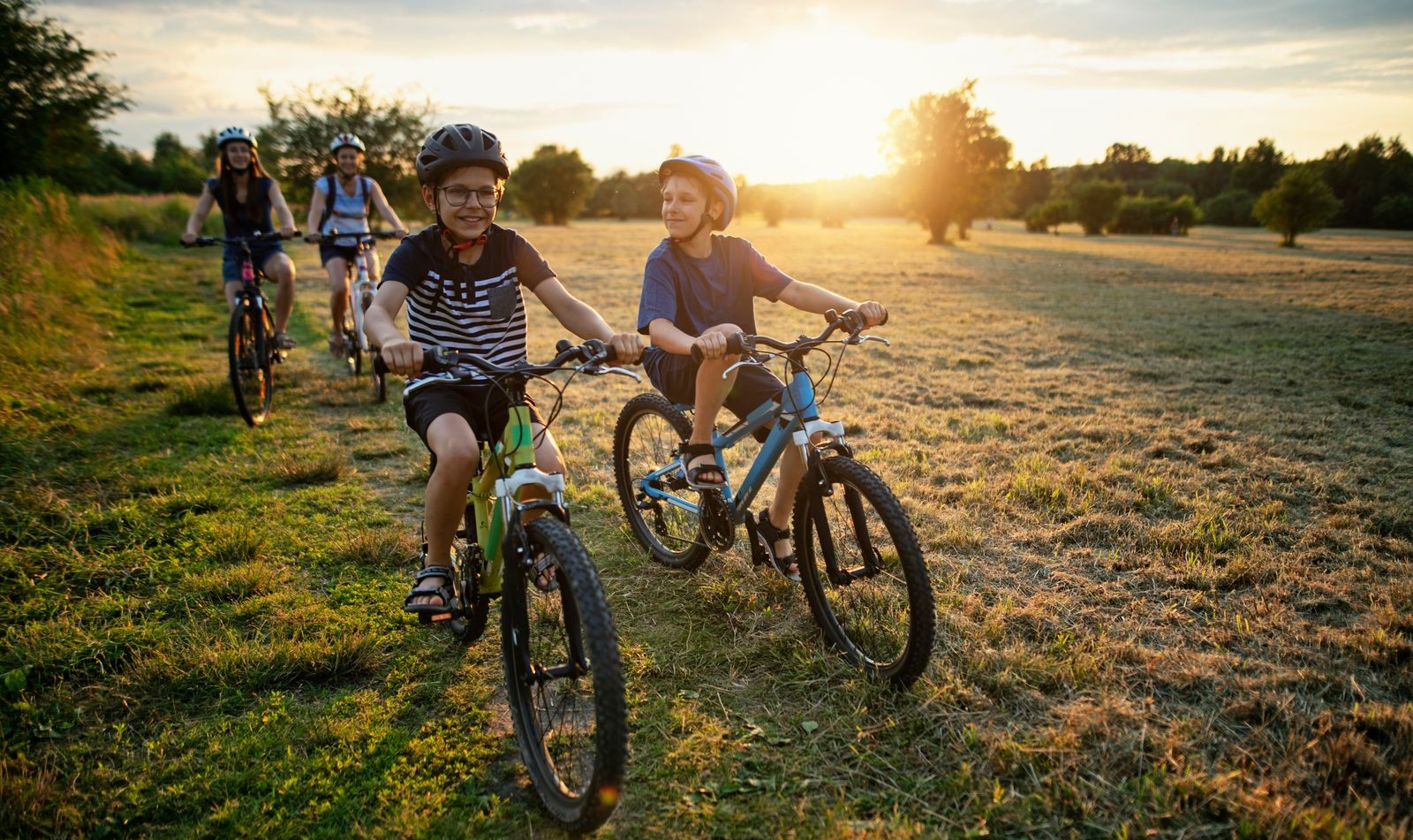 Family biking through a sunlit field with warm light in the background, reflecting the active, outdoor lifestyle of life at Pasadena Ridge.